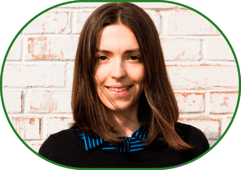 Великий план, портрет. На тлі білої цегляної стіни жінка з довгим каштановим волоссям, що злегка розвівається від вітру, привітно дивиться карими очима в кадр і всміхається. З-під чорного светра визирає комірець синьої сорочки.